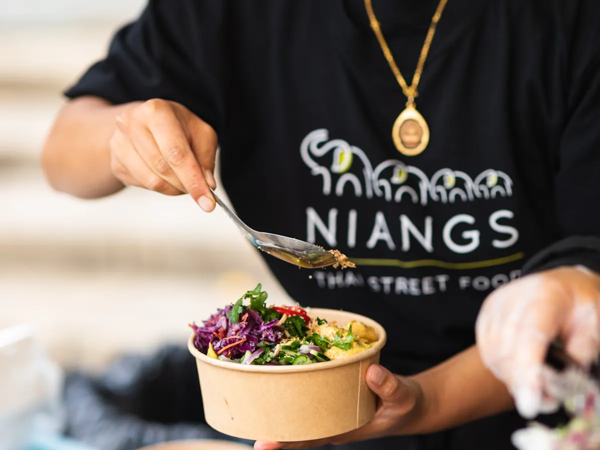 Niang's Thai Street Food team member serving a fresh curry box at the market stall