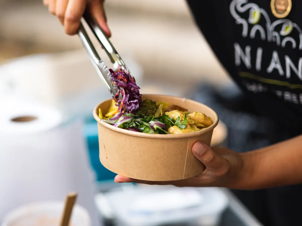 Niang's Thai Street Food team member garnishing a curry box with fresh red cabbage